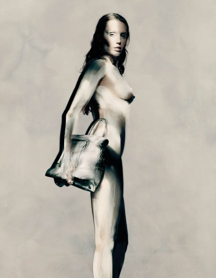 A model with striking body paint holding a handbag in a Maison Margiela campaign, showcasing bold fashion artistry.