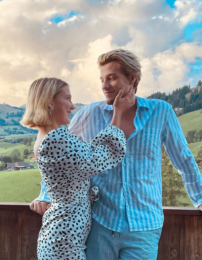 Millie Bobby Brown and Jake Bongiovi smiling outdoors in a scenic landscape, showing their affectionate moment together.