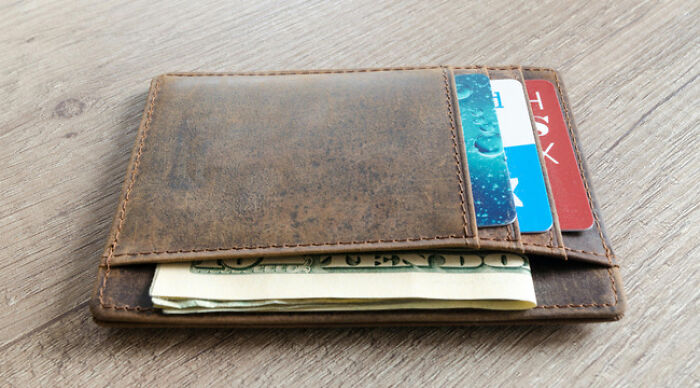 Brown leather wallet on wooden surface holding cash and multiple cards, illustrating the moral dilemma poll concept.