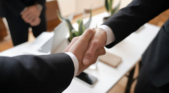 Two people in business suits shaking hands during a moral dilemma poll discussion in an office setting
