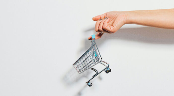 Hand holding a miniature shopping cart against a white background illustrating the moral dilemma concept.