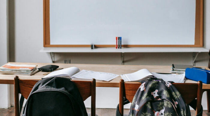 Classroom with backpacks on chairs and open notebooks on desks, setting for a moral dilemma poll or quiz.