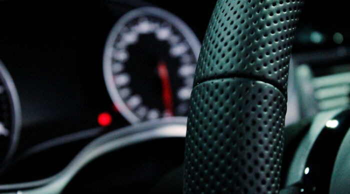 Close-up of a perforated leather steering wheel in a car with a blurred speedometer in the background, moral dilemma concept.