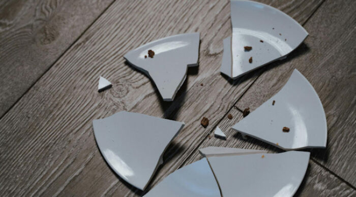 Broken white ceramic plate on wooden floor symbolizing moral dilemma in am I the problem poll concept