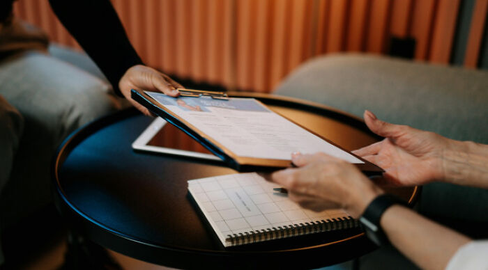 Two people discussing a moral dilemma poll questionnaire on a clipboard at a small round table.