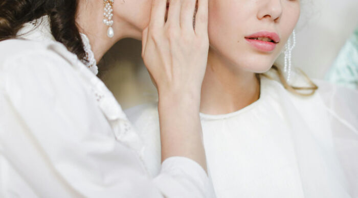 Two women in white dresses, one whispering a secret to the other, illustrating a moral dilemma poll concept.