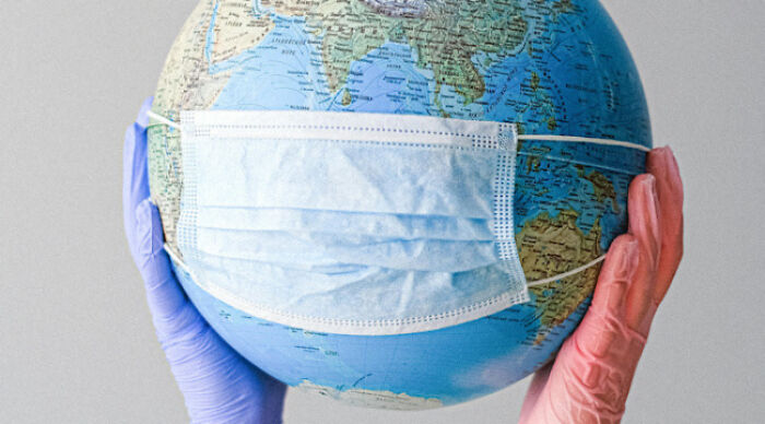 Hands wearing gloves hold a globe with a medical mask, symbolizing moral dilemma poll and global responsibility questions.