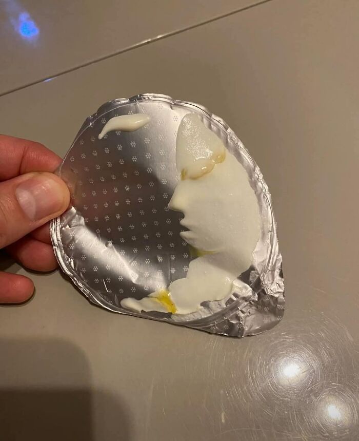 Hand holding foil lid with cream shaped like a side profile face, an example of random objects that look like faces.