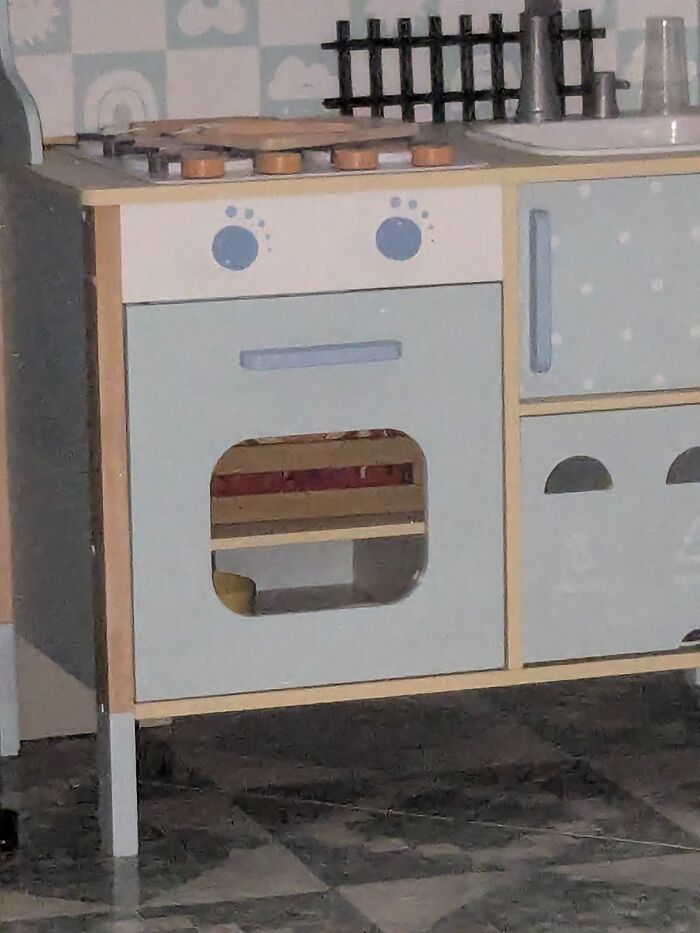 Toy kitchen with random objects that look like faces, showing a surprised expression on the oven door panel.
