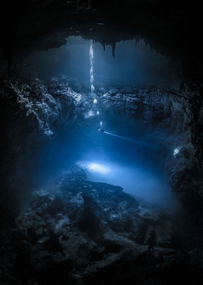 Underwater cave illuminated by a diver's light beam in a stunning ocean photography image from Photographer of the Year awards.