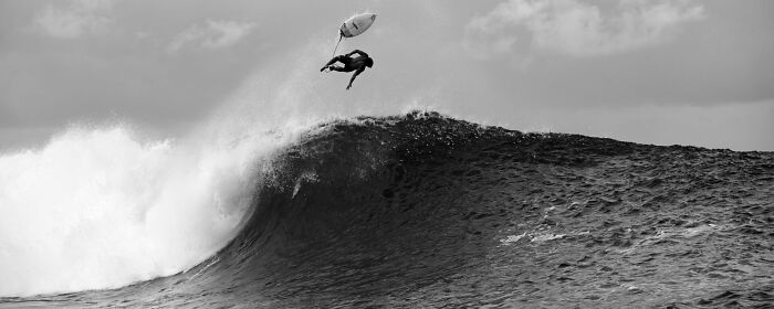 Surfer performing an aerial maneuver above a large wave, captured in a stunning ocean photography moment.