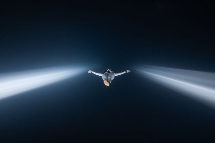 Underwater diver illuminated by beams of light in a dark ocean scene from Ocean Photographer of the Year Awards.