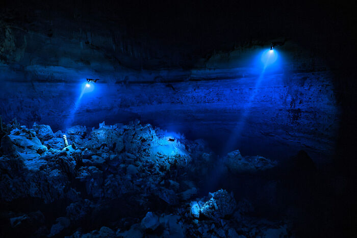 Two divers with underwater lights exploring a deep ocean cave, showcasing stunning ocean photography.