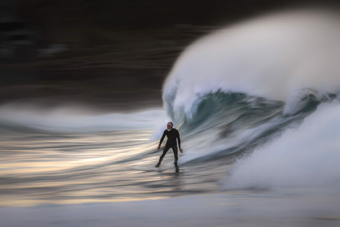 Surfer riding a large wave at sunset captured in a dynamic ocean photographer of the year awards image.