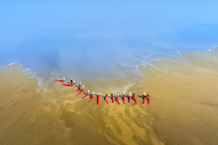 Aerial view of people wearing red gear walking in shallow water at Ocean Photographer of the Year awards.