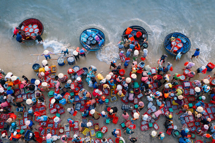 Aerial view of fishermen and locals with round boats sorting fish on the shore, showcasing stunning ocean photography.