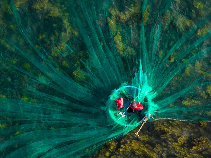 Aerial view of fishermen casting large green nets in the ocean, captured for ocean photographer of the year awards.
