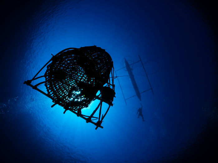 Underwater view of a deep-sea trap and a diver near a boat, showcasing ocean photography from the 2025 awards.