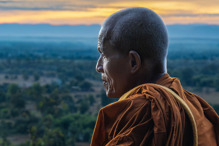 Profile of a monk wearing traditional robes overlooking a vast natural landscape, showcasing cultural beauty captured by a photographer.