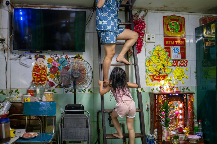 Child helping adult climb wooden ladder inside colorful Asian home, capturing the beauty of cultures in travel photography.