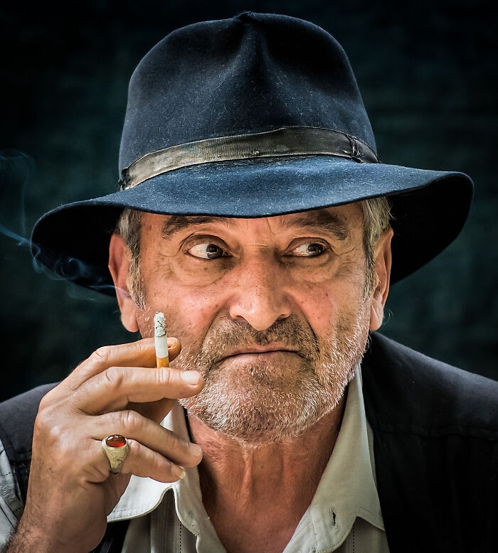 Older man smoking cigarette wearing a black hat, captured by a photographer showcasing the beauty of cultures worldwide.