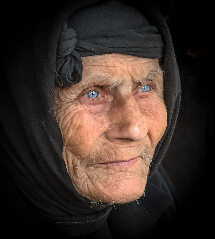 Elderly woman with bright blue eyes wearing traditional black headscarf, showcasing cultural beauty captured by photographer.