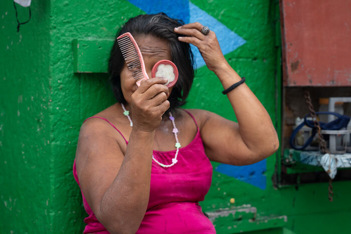 Woman in a pink dress fixing her hair with a comb while holding a small mirror, showcasing cultural beauty captured by photographer.