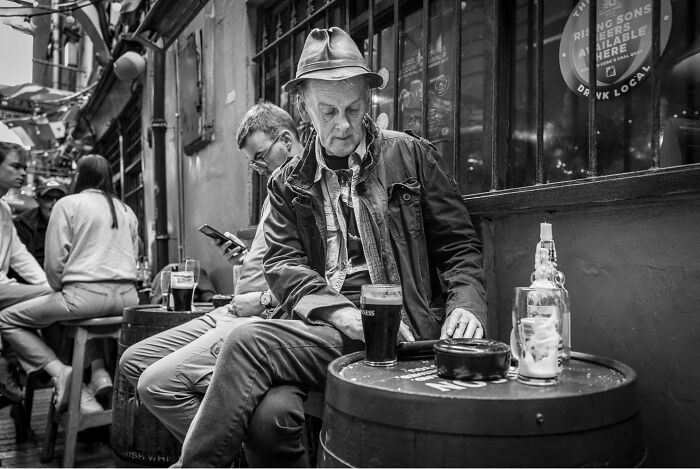Man in hat sitting at outdoor pub table with a pint, illustrating striking photographs capturing the hidden poetry of everyday life.