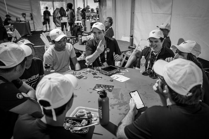 Group of men wearing caps playing cards and sharing moments, capturing the hidden poetry of everyday life in black and white.
