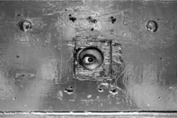 Close-up black and white photo showing an eye peering through a small hole in a weathered surface, capturing hidden poetry.