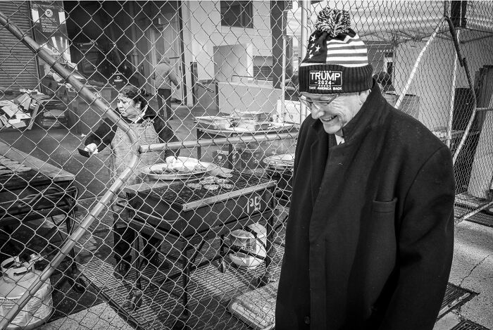 Black and white photograph capturing the hidden poetry of everyday life with two men near a fenced area.