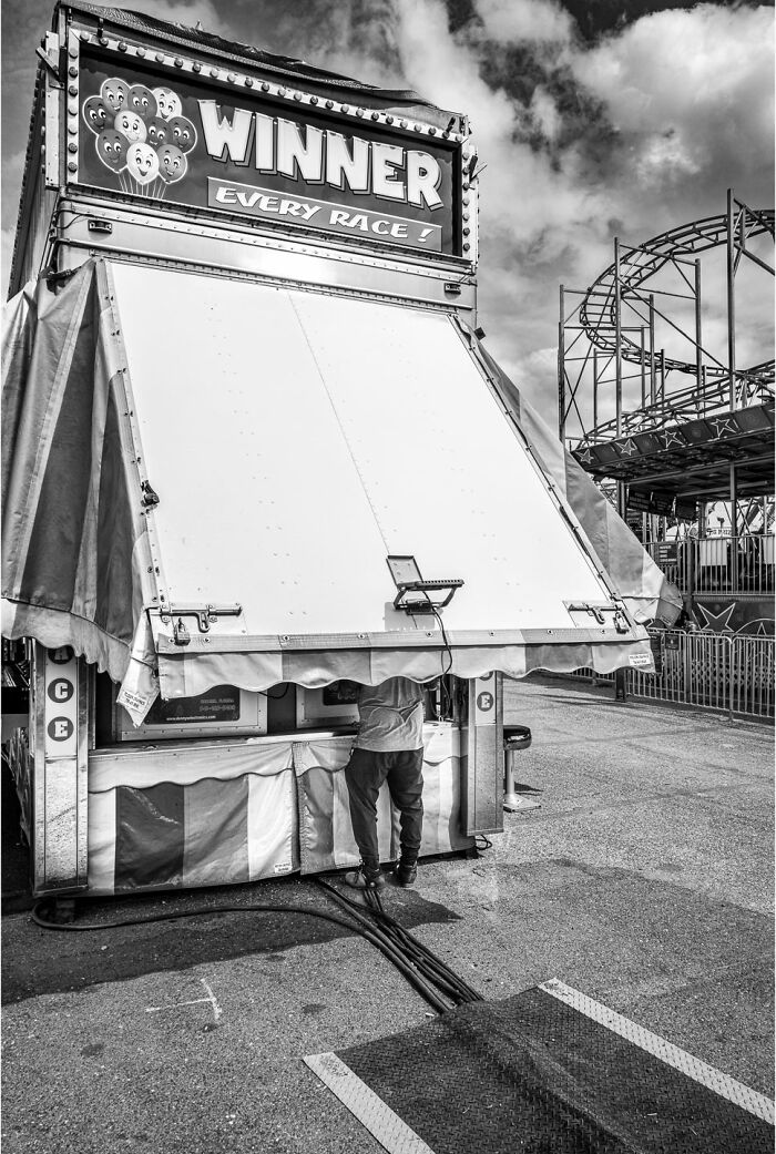 Black and white photograph capturing the hidden poetry of everyday life at a carnival game booth closing time.