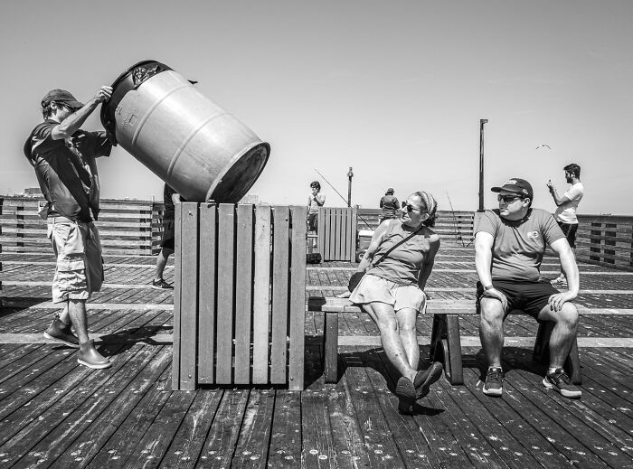Black and white photograph capturing the hidden poetry of everyday life with people relaxing and interacting on a wooden pier.