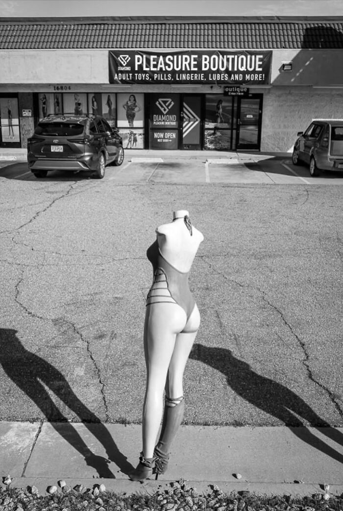Mannequin in lingerie outside an adult boutique with cars in parking lot, capturing the hidden poetry of everyday life.