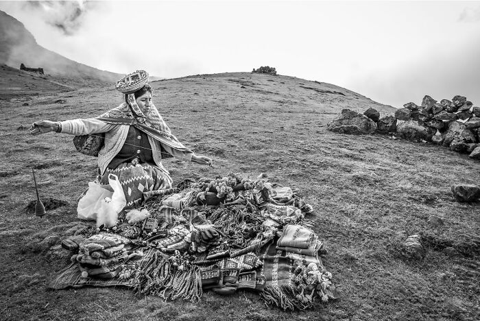 Woman in traditional clothing arranging textiles on a hillside, capturing the hidden poetry of everyday life in a striking photograph