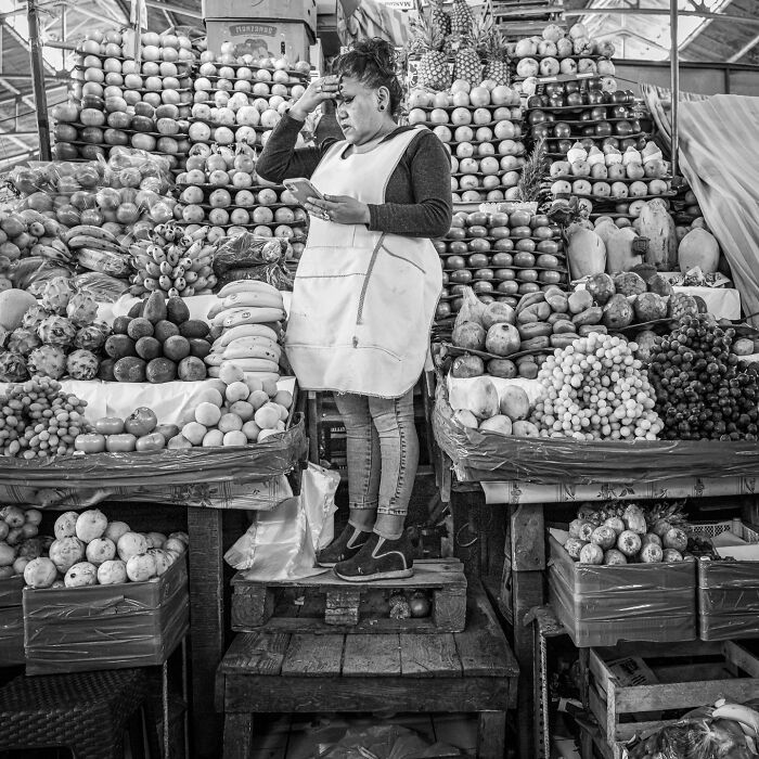 Woman selling fruits at a market stall, surrounded by neatly arranged fresh produce, capturing the hidden poetry of everyday life.