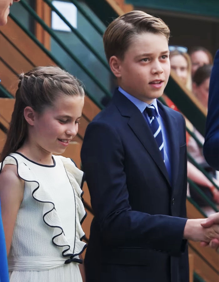 Prince George dressed in a suit, shaking hands at an event, with a young girl beside him, spotlight on future king. Prince George dressed in a suit, shaking hands at an event, with a young girl beside him, spotlight on future king.