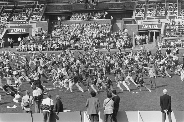 Large group of people participating in a coordinated activity on a stadium field in a historical photo.