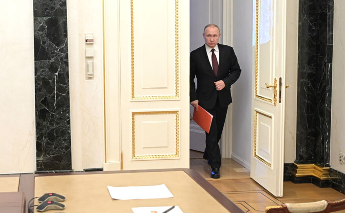 Vladimir Putin entering a room holding a folder, sparking discussions about his twitching leg and exoskeleton rumors.