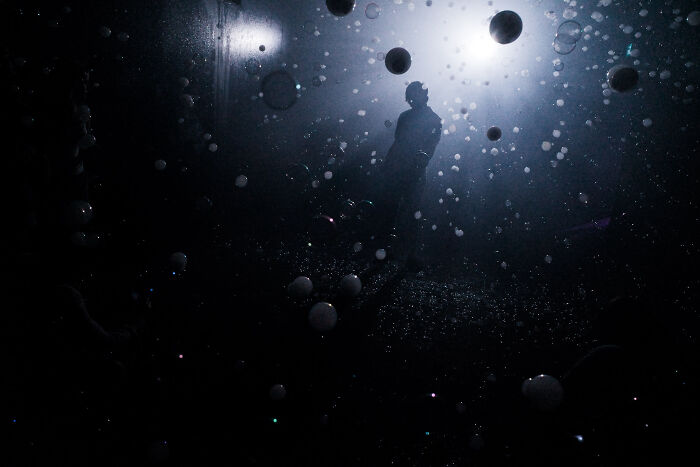 Silhouetted figure surrounded by floating spheres in a dark, cinematic scene captured by a photographer.