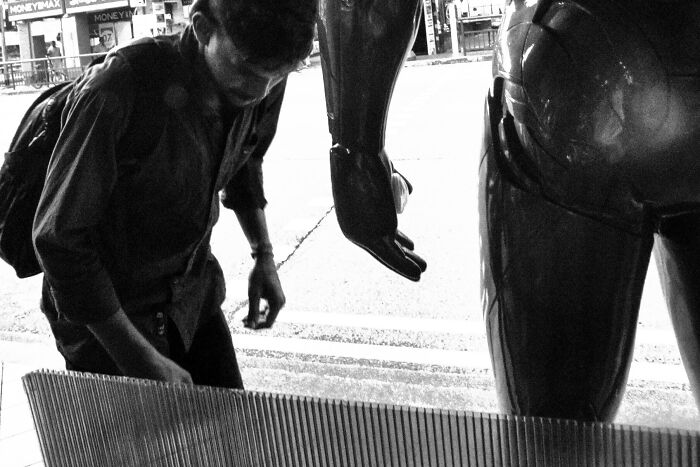 Black and white cinematic image of a photographer capturing an ordinary moment with artistic framing on a city street.