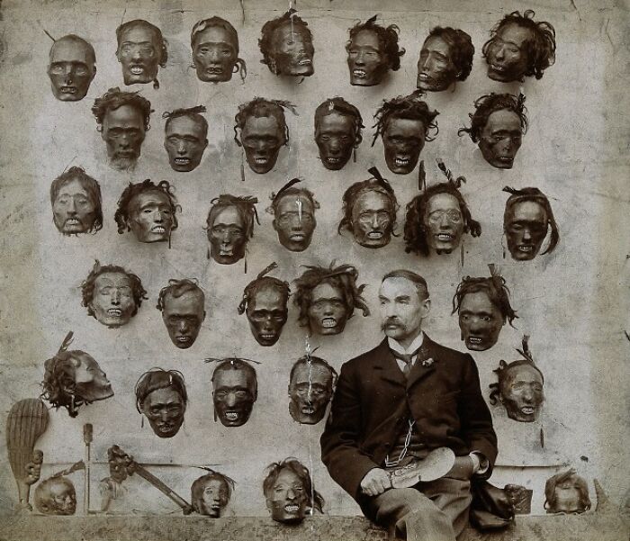 Man seated next to a wall displaying multiple unsettling severed heads, creating a creepy and chilling captured moment.