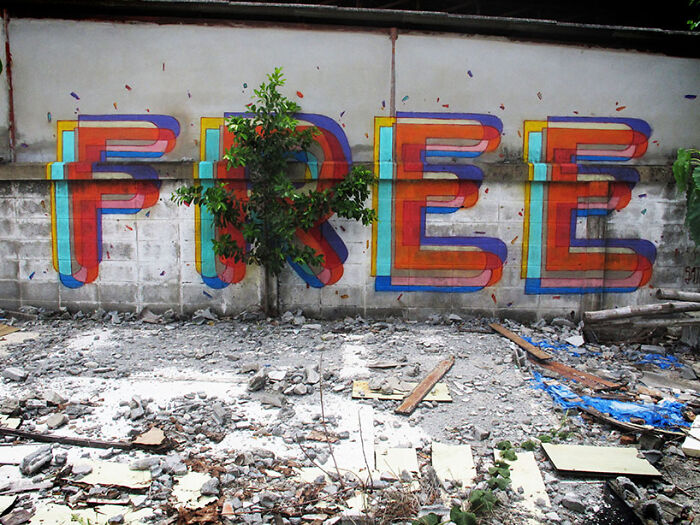 Colorful street art spelling free on a wall with a small tree growing through the letter R in an urban outdoor setting.
