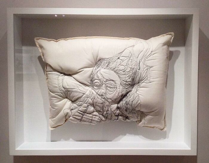 Embroidered pillow art by Maryam Ashkanian featuring a detailed face design, capturing the beauty of sleep in soft fabric.