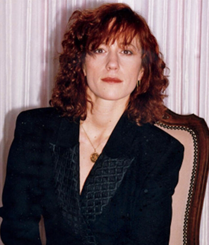 Woman with curly red hair and black blazer seated in a vintage chair related to world’s greatest unsolved mysteries topic.