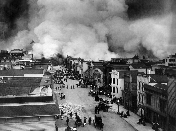 Black and white historical photo of a city street with smoke billowing from buildings during a large fire event.