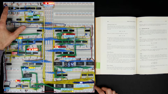 Hands working on a fully functional 8-bit computer built from K’Nex parts with wires, LEDs, and an open programming book nearby Hands working on a fully functional 8-bit computer built from K’Nex parts with wires, LEDs, and an open programming book nearby