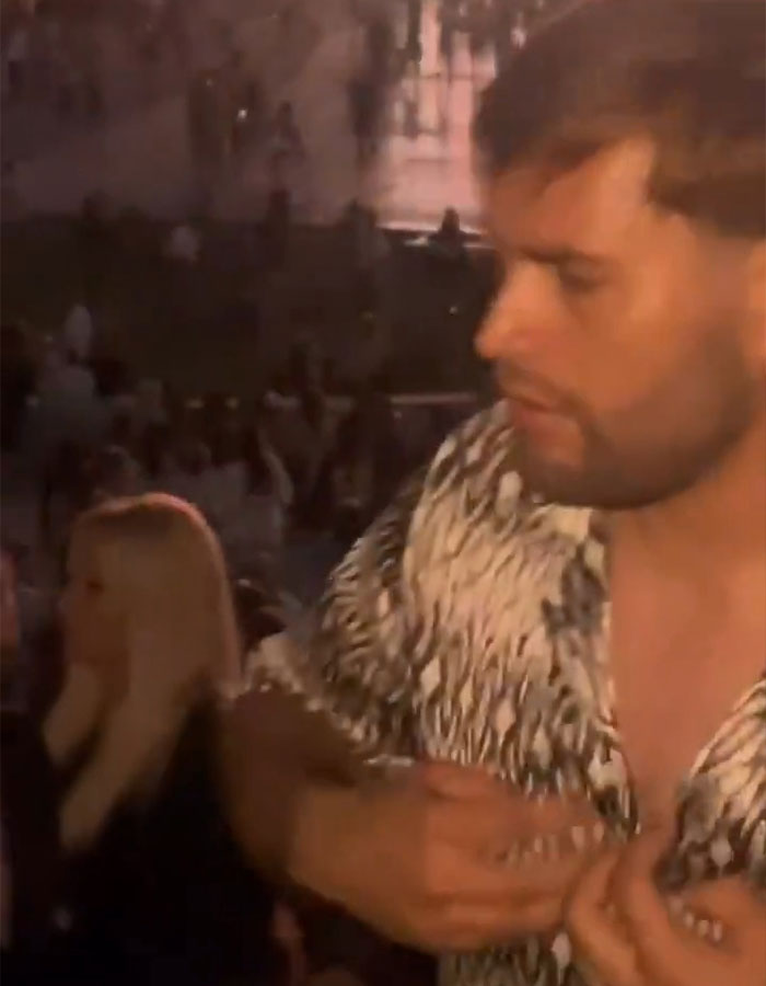 Man at concert adjusting shirt while crowd watches, related to mom punched unconscious after drink incident.