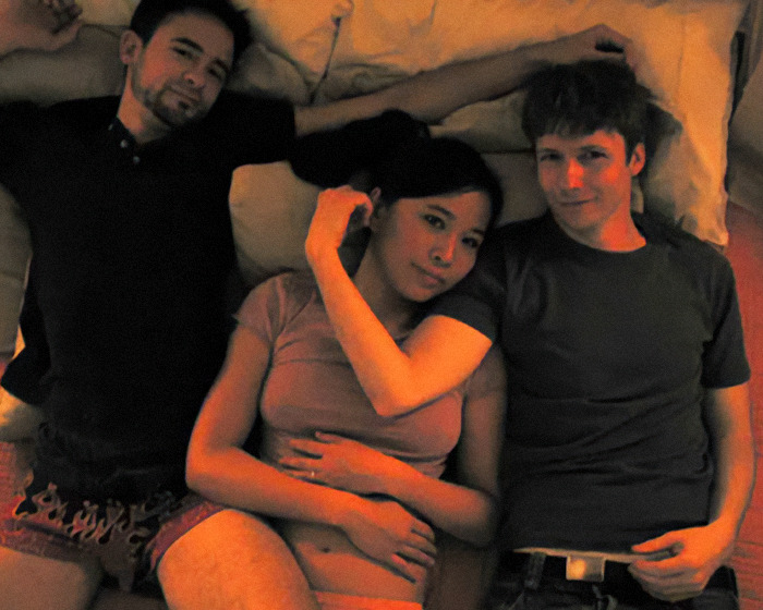 Three movie stars lying closely on a bed, illustrating moments of love-making scenes during filming.