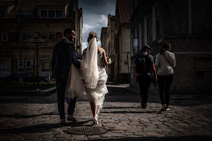 Bride and groom walking on cobblestone street with two pedestrians, capturing the beauty of cultures in a travel photo.